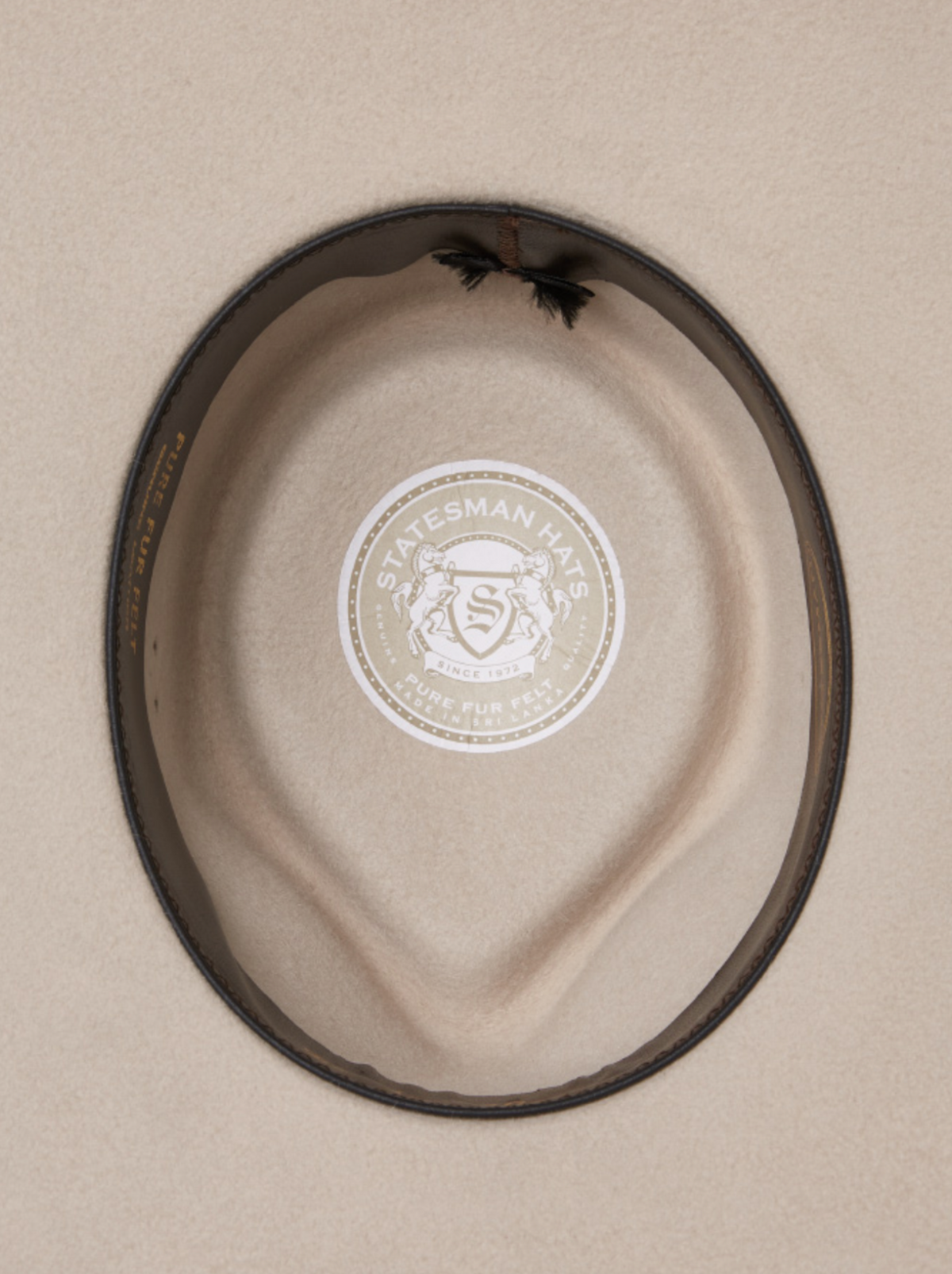 A top-down view of the Statesman Big Australian Fur Felt Hat in beige, featuring a brown leather band. Inside, the lining displays a circular "Statesman Hats" logo with two lions and the words "Pure Fur Felt.