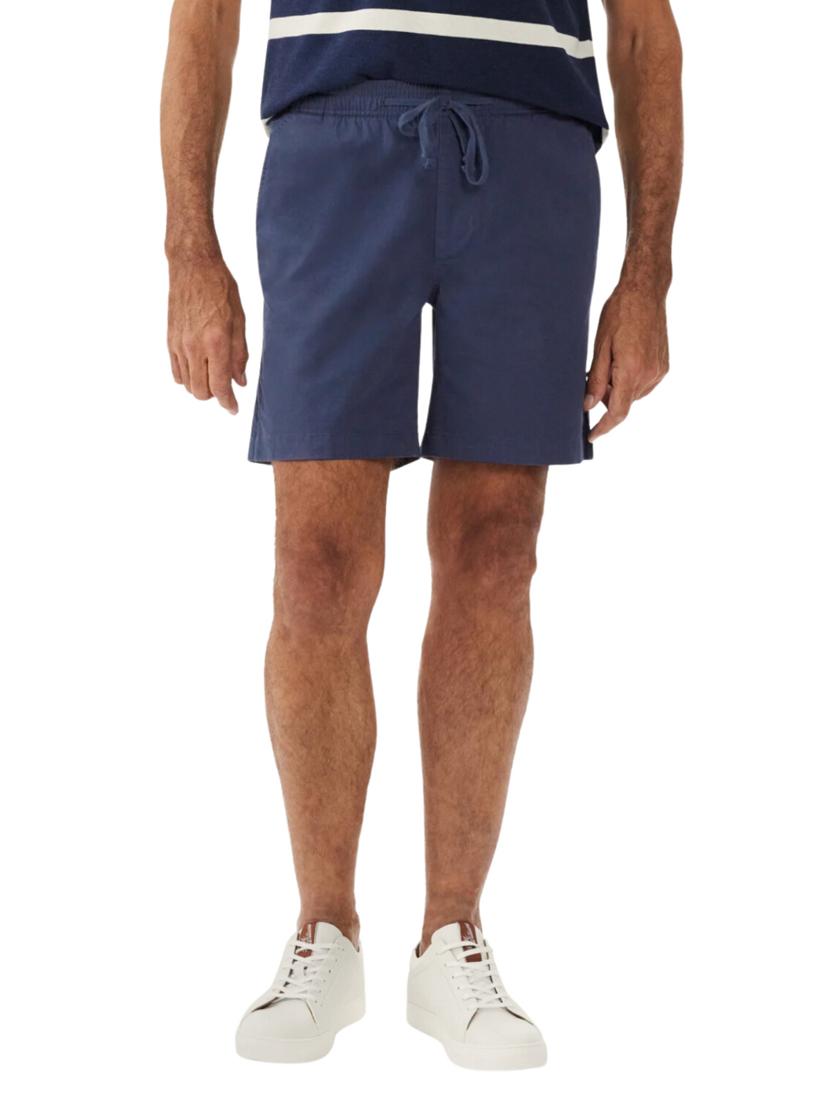 A person wearing RM Williams R.M.W Rugby Shorts in navy blue stretch cotton twill stands with their arms relaxed at their sides. The individual is also wearing a blue and white striped shirt and white sneakers, embodying a relaxed style against the plain white background.