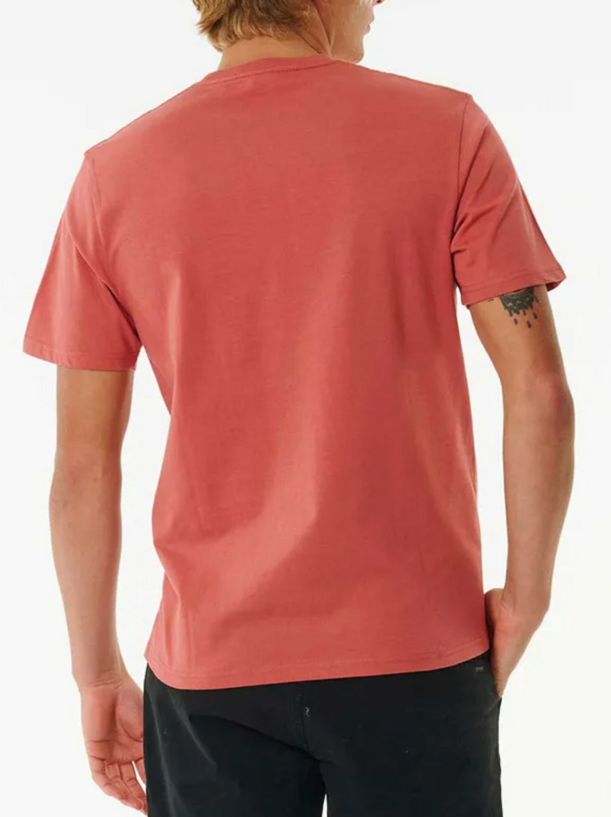 A person with light hair is depicted from the back, casually standing against a white background. They're wearing a classic staple: the red Rip Curl Plain Pocket Tee with short sleeves and black pants, revealing a small tattoo on their left arm.