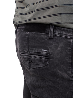 Close-up of a person wearing Industrie The Drifter Denim Short in faded black, showing the back pocket with a button and a small brand tag above it, paired with a green striped shirt tucked in.
