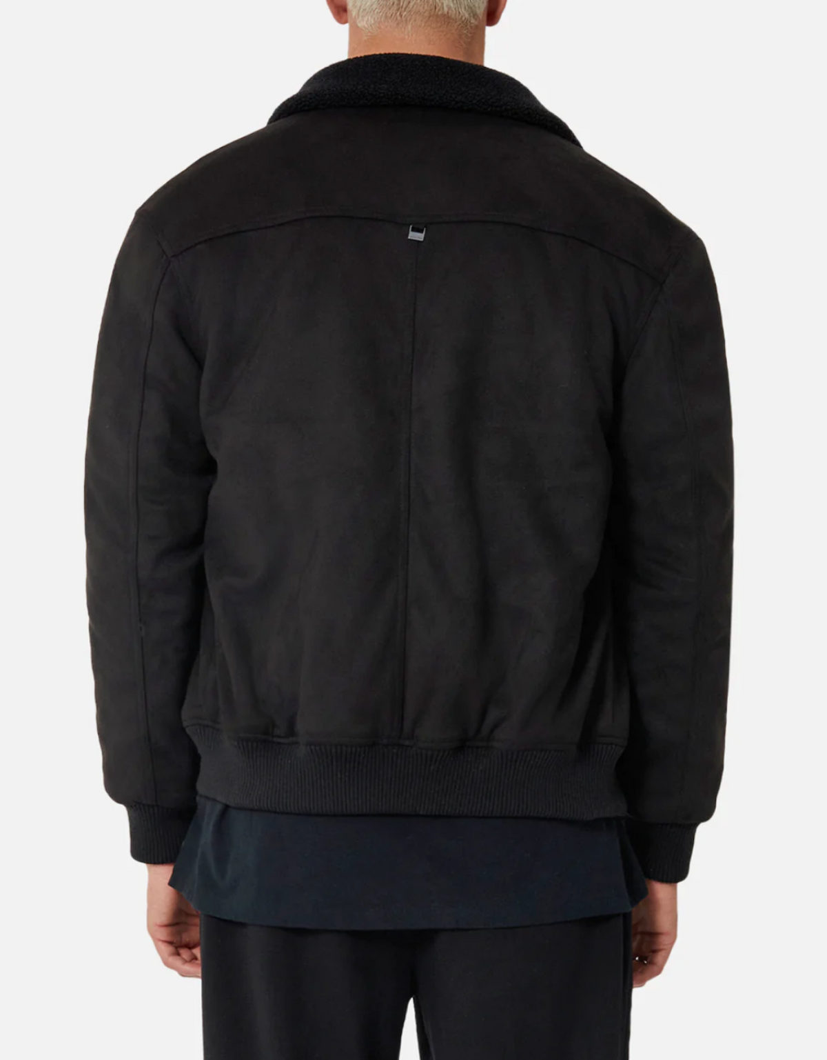 A person wearing the Industrie The Mig Jacket, a black bomber-style jacket with a ribbed waistband and faux sherpa collar, shown from the back over a long black shirt and black pants.