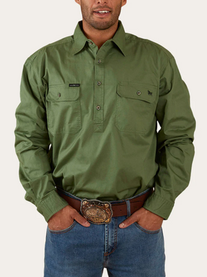 A person stands against a plain background wearing an olive-green Ringers Western King River Half Button Shirt with two chest pockets. They have their hands in the pockets of their blue jeans, which are accessorized with a large ornate belt buckle.