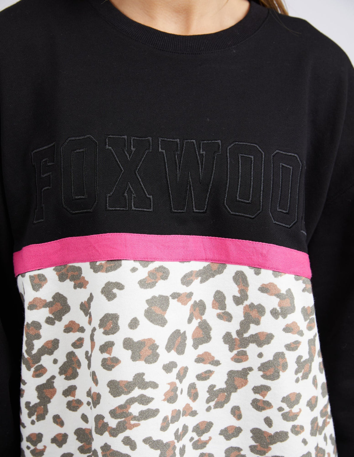 Wearing the Foxwood Split Crew—a crew neck sweater with bold "FOXWOOD" text, a pink stripe, and a white panel featuring brown and black leopard print—adds a stylish touch to any casual outfit.