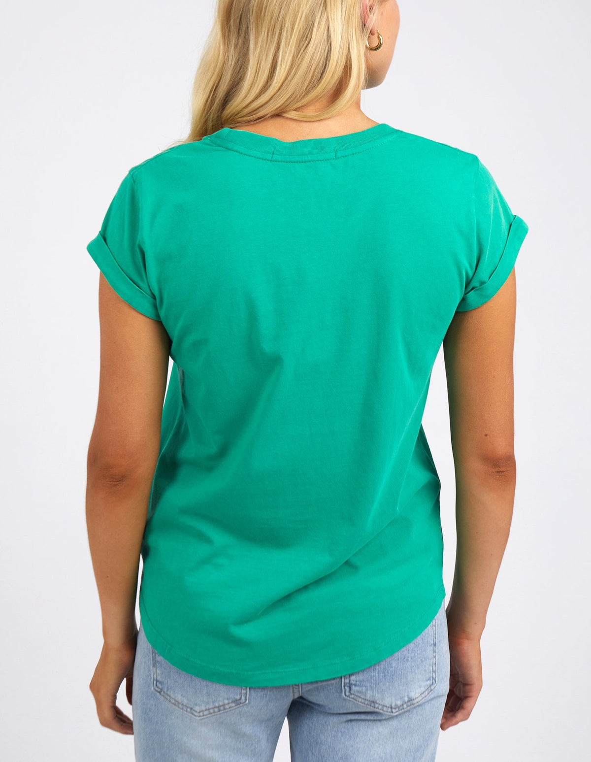 A person with long blonde hair is seen from the back wearing a green Foxwood Signature Tee and light blue jeans, set against a plain background.