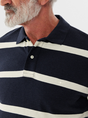 A gray-bearded man wears an RM Williams Rod Polo, featuring cotton pique fabric in navy and white stripes with detailed longhorn embroidery on the chest. The image centers on his upper body, showcasing the shirt's pattern and texture.