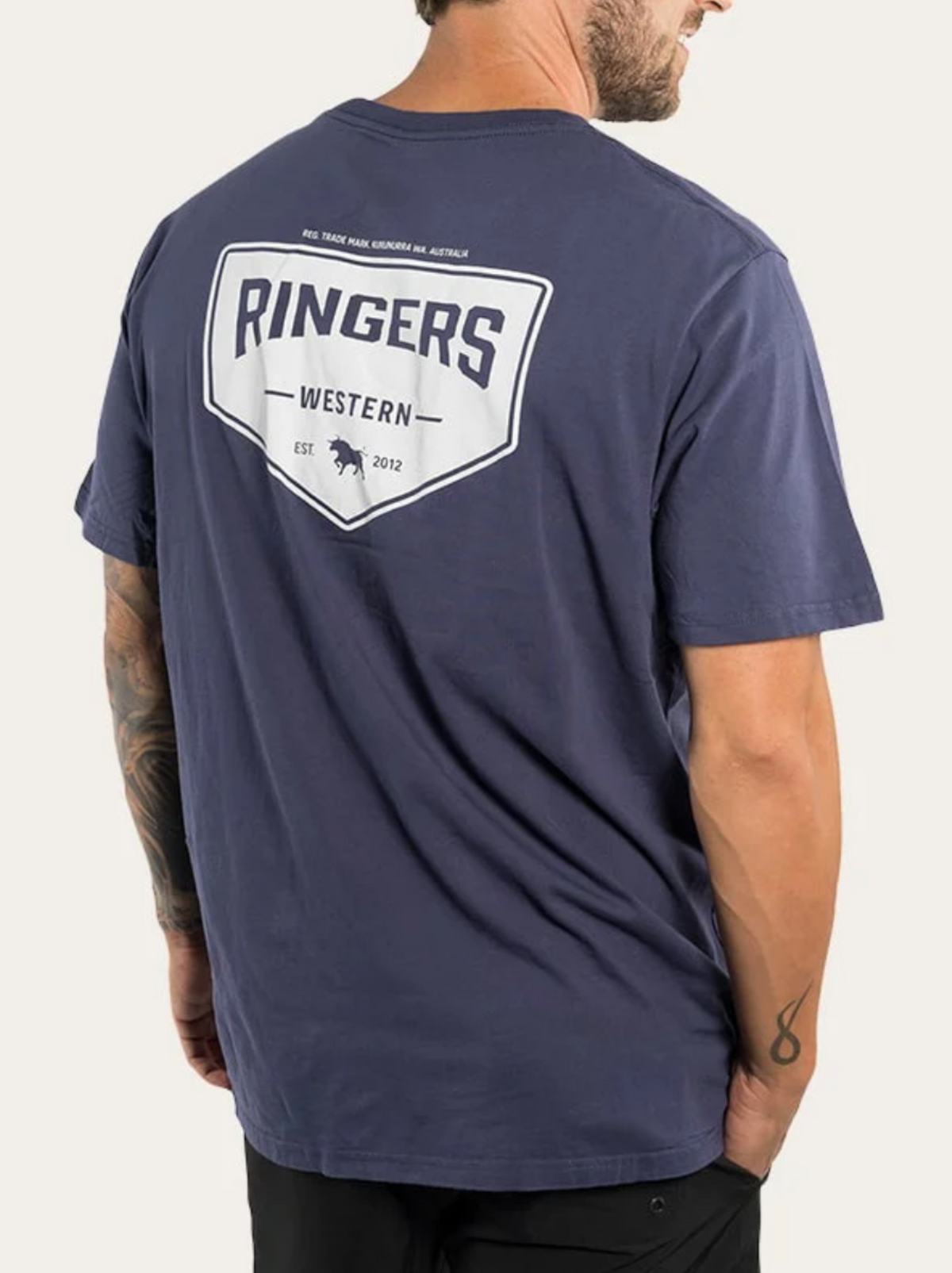 A man in a navy blue Ringers Western Squadron Loose Fit T-Shirt, made from 100% cotton jersey with a white logo and text on the back, stands with his back to the camera and looks over his left shoulder.