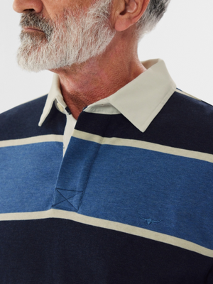 An older man with a white beard wears the RM Williams Tweedale Rugby shirt in navy and blue stripes, crafted from heavyweight jersey knit. It features subtle longhorn embroidery on the chest, set against a plain white background that highlights his classic style.