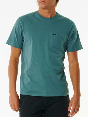 A person wears the Rip Curl Plain Pocket Tee—100% cotton, teal, short sleeves—paired with dark pants, standing against a plain white background.