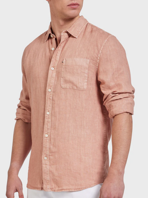 A man wears the Academy Brand Hampton Linen Shirt in light pink, featuring long sleeves with a chest pocket. The linen shirt's sleeves are rolled up as he stands slightly turned against a plain background.