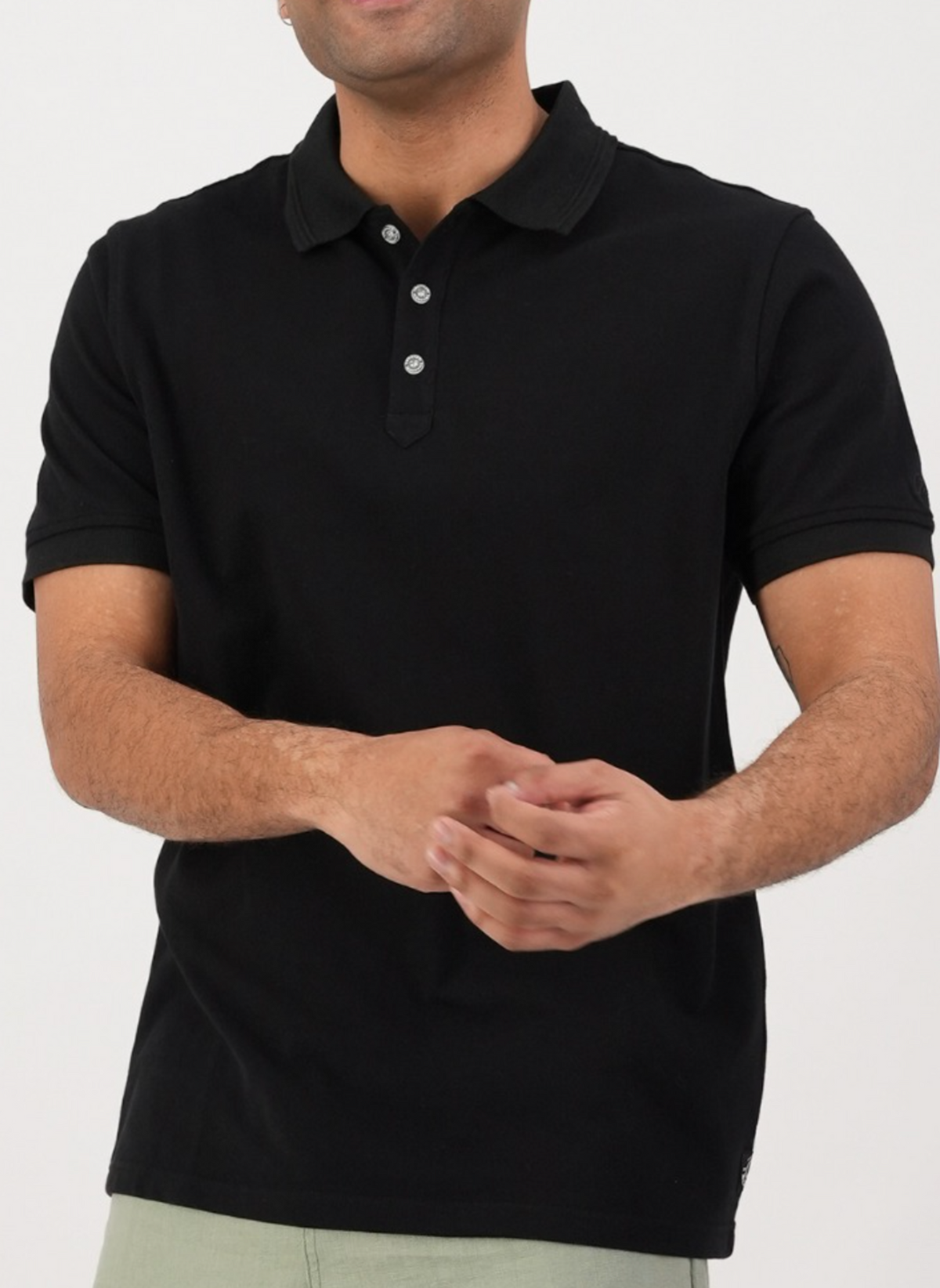 A person is wearing a black Swanndri Highgrove Polo in cotton pique, with a collar and three buttons, paired with light pants, set against a white background.