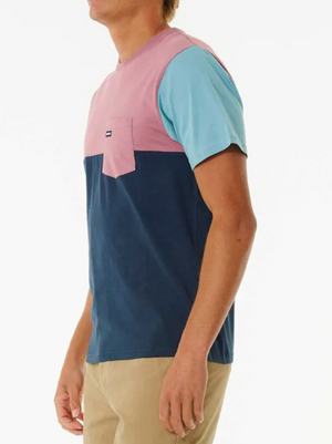 A man wears the Rip Curl Surf Revival Custom Tee, a 100% cotton t-shirt with pink, blue, and navy color-blocked sections, paired with tan pants against a white background for a casual style.