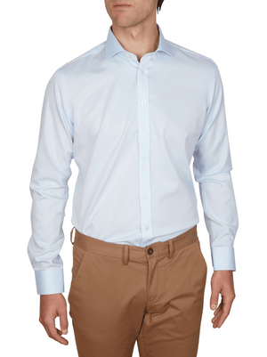 A man wears the Abelard Non Iron Cotton Twill Slim Fit Shirt in light blue with a cutaway collar and light brown pants, standing relaxed with arms at his sides and facing forward. The image is cropped just above his head.