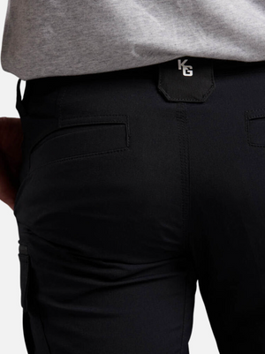 A close-up of a person wearing black King Gee Trademark Cargo Shorts and a grey shirt, highlighting the back pocket area with a small black "KG" tag.