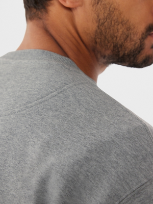 A close-up of a man's shoulder and back of the head in an RM Williams R.M.W Script Crew Neck, showcasing the grey cotton blend fabric's texture and stitching with R.M.Williams embroidery against a plain white background.