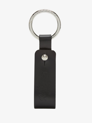 The RM Williams Pioneer Key Fob is crafted from black double butt leather with a silver metal ring. It features a vertical strap secured by nickel hardware in a silver button shape, and the leather is subtly embossed with indiscernible text.