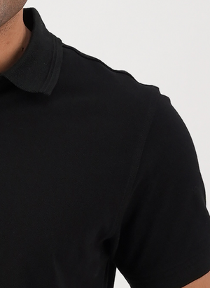 Close-up of a person wearing the Swanndri Highgrove Polo in black, highlighting its classic style and cotton pique texture, with the shot focusing on their upper left chest and shoulder against a plain white background.