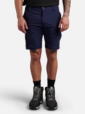 A person in navy King Gee Trademark Cargo Shorts made of stretch ripstop fabric, black socks, and black hiking boots stands against a white background. They also have a tattooed left arm and wear a black t-shirt.