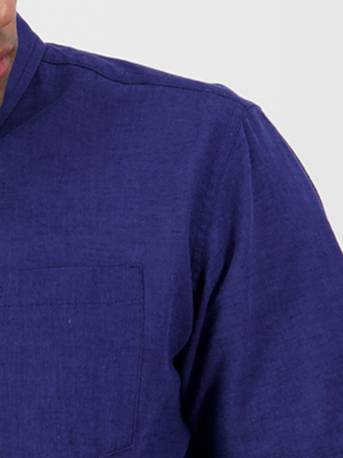 A close-up of a person wearing the Swanndri Lowell v2 Short Sleeve Shirt in blue, featuring a button down collar and chest pocket. Only the shoulder, partial chest, and collar are visible against a plain light background.