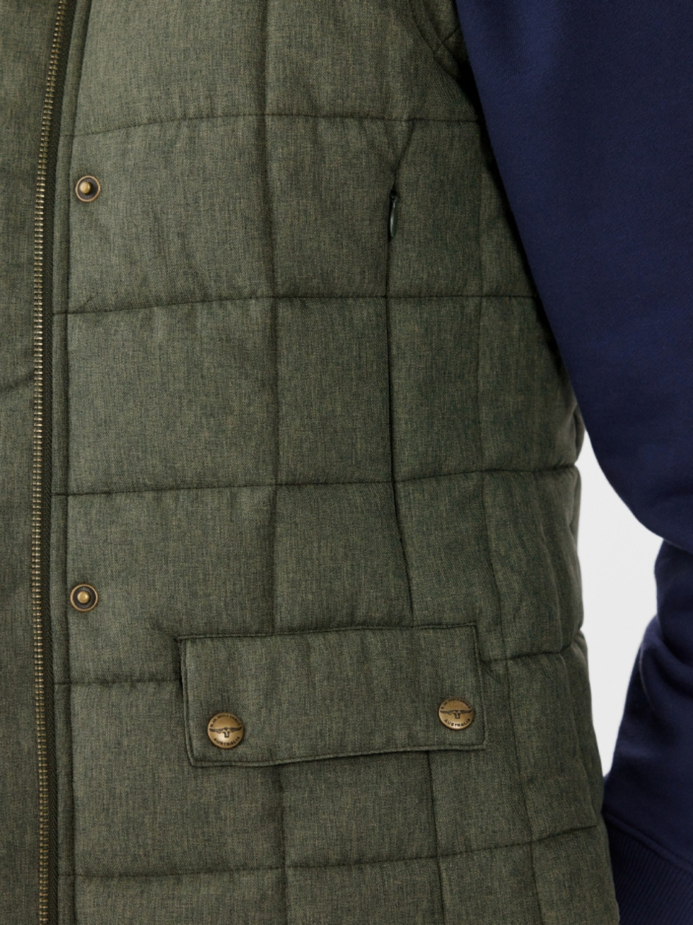 Close-up of a person wearing the RM Williams Wilpena Creek Vest, a quilted green piece crafted from recycled polyester with pocket and button details, over a navy long-sleeve shirt. The sporty vest is partially zipped, highlighting its textured fabric.