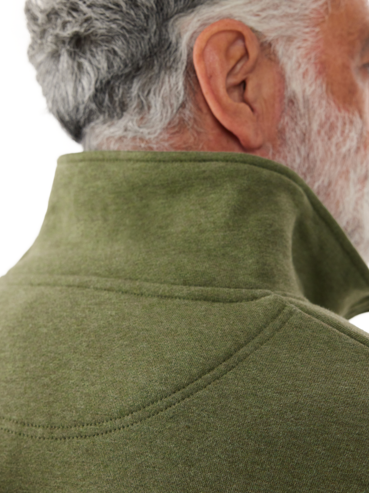 Close-up of an older man's head and shoulder in profile, highlighting his gray hair and beard. He is wearing a RM Williams Mulyungarie Fleece jacket in green with a high collar, featuring a vintage-inspired leather patch, emphasizing the texture and color of the cotton fleece.