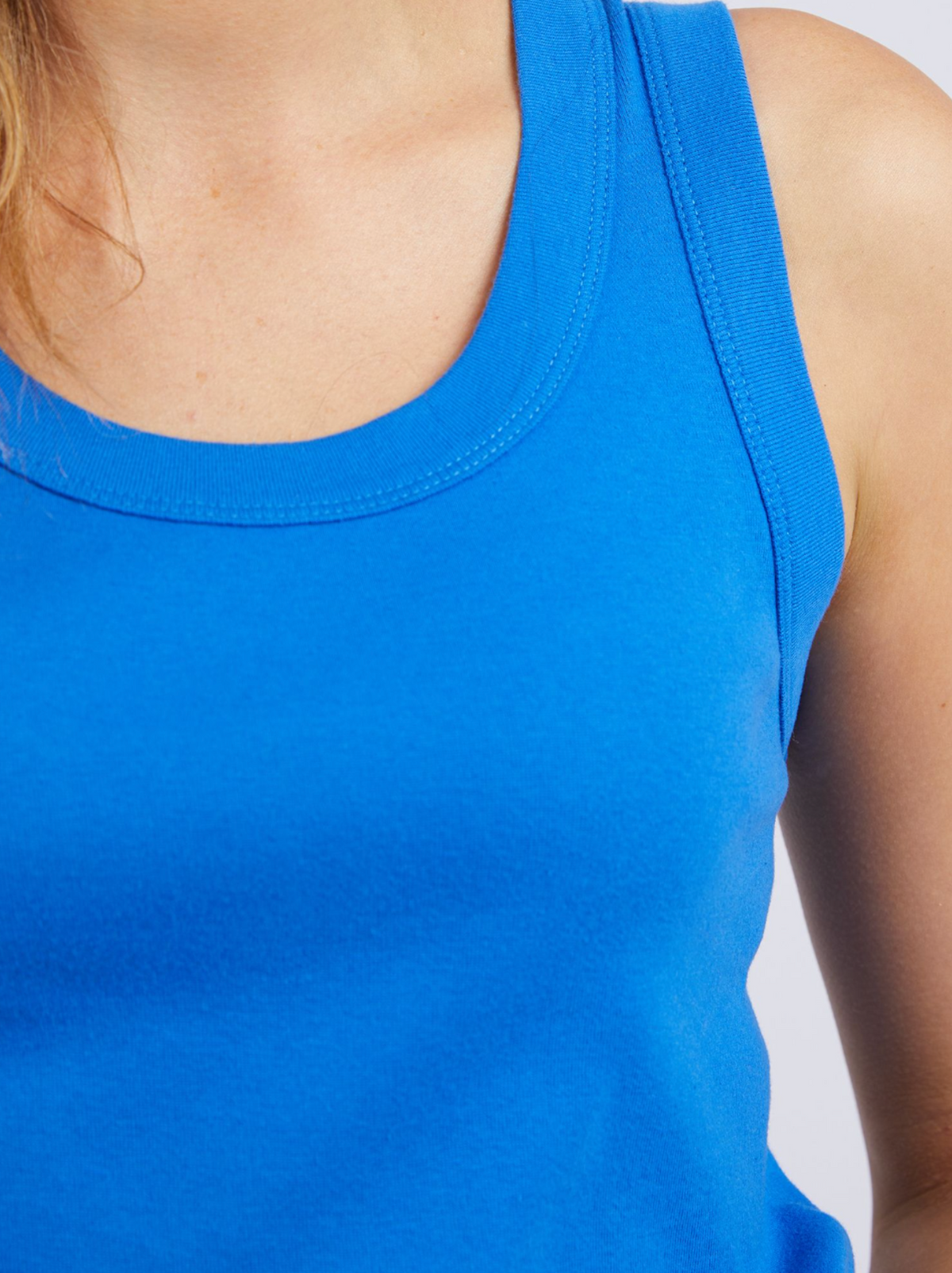 Close-up of a person in the Foxwood Esme Tank, a stylish rib knit top in bright blue, highlighting the upper chest, shoulder, and neck with light skin and blonde hair against a plain light background.