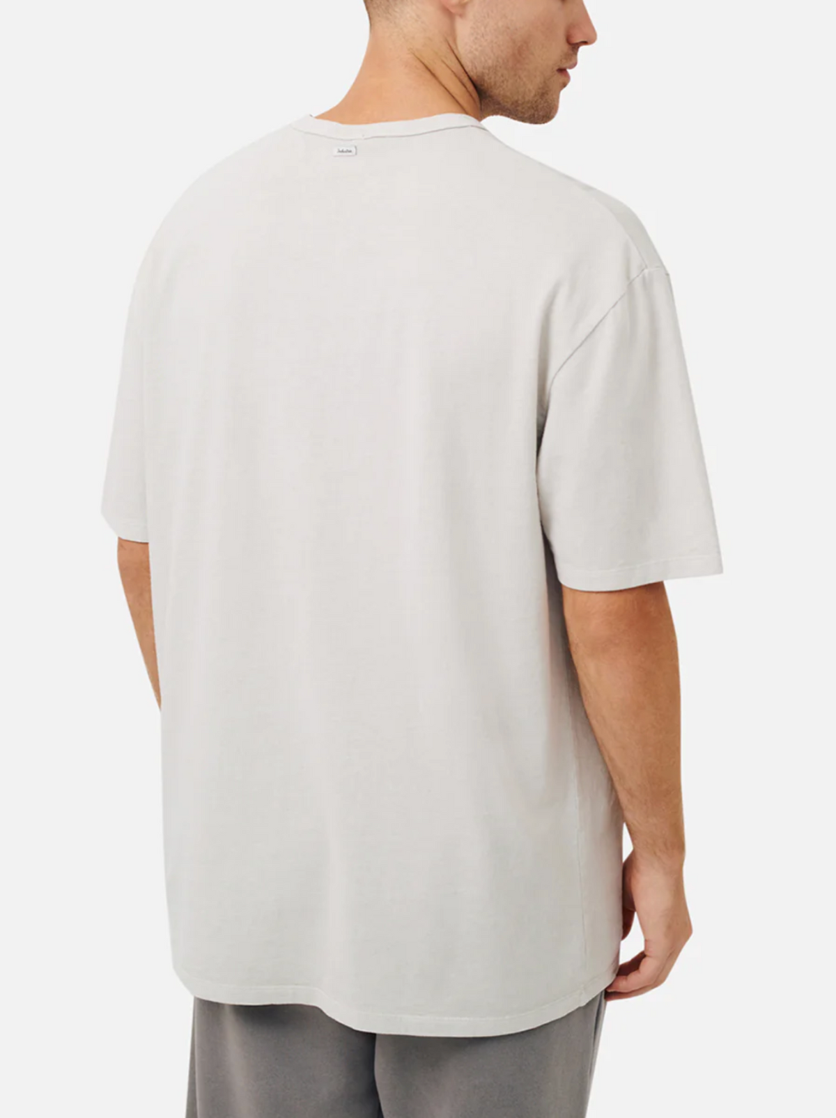 A man is seen from behind wearing the Industrie The Del Sur Tee in light grey, made from 100% cotton with an oversized fit, short sleeves, and a round neckline. He pairs it with grey pants against a plain white background.