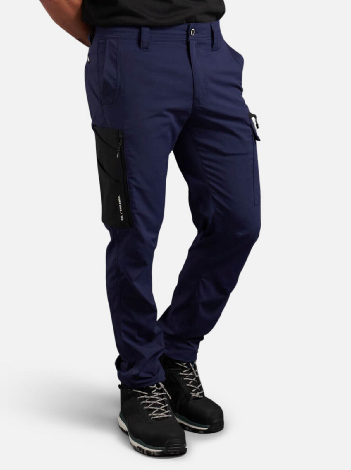 A person is wearing navy King Gee Trademark Cargo Pants featuring side pocket details and black hiking boots, crafted from durable ripstop fabric. They stand against a plain white background with their hands behind their back.