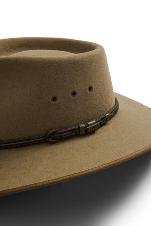 Close-up of a tan Akubra Cattleman hat featuring a brown braided band, metal "Akubra" tag, ventilation eyelets, and wide brim—perfect for outdoor adventurers seeking rugged sophistication.