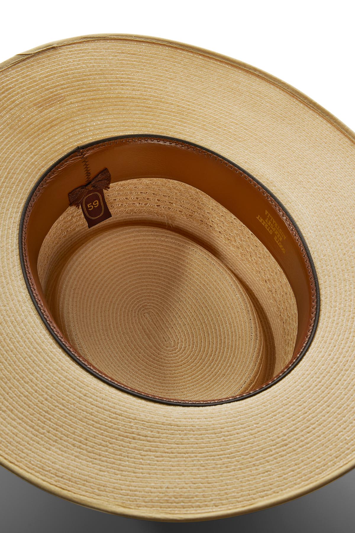 Top-down view of the Akubra Byron Straw Hat's interior showing a brown leather inner band with small gold brand details and a size tag marked “59,” set against a plain background.