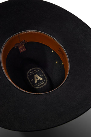 Close-up of the inside of an Akubra Riverina hat in black felt, featuring a brown leather sweatband, logo lining with "A", "HATTER", "1876", and a visible size 57 tag. Offers both classic style and sun protection.