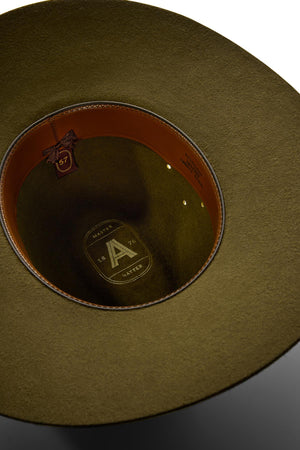 Close-up of the inside of an olive green Akubra Riverina hat, featuring a brown leather sweatband, gold size tag marked "57," and embossed inner crown branding—crafted for sun protection with its broad brim.
