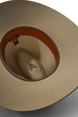 A close-up of the Akubra Riverina cowboy hat’s beige interior shows a brown leather sweatband, size tag, and logo with "A," "HATTER," and "MASTER 1875"—a comfortable, stylish option for sun protection.