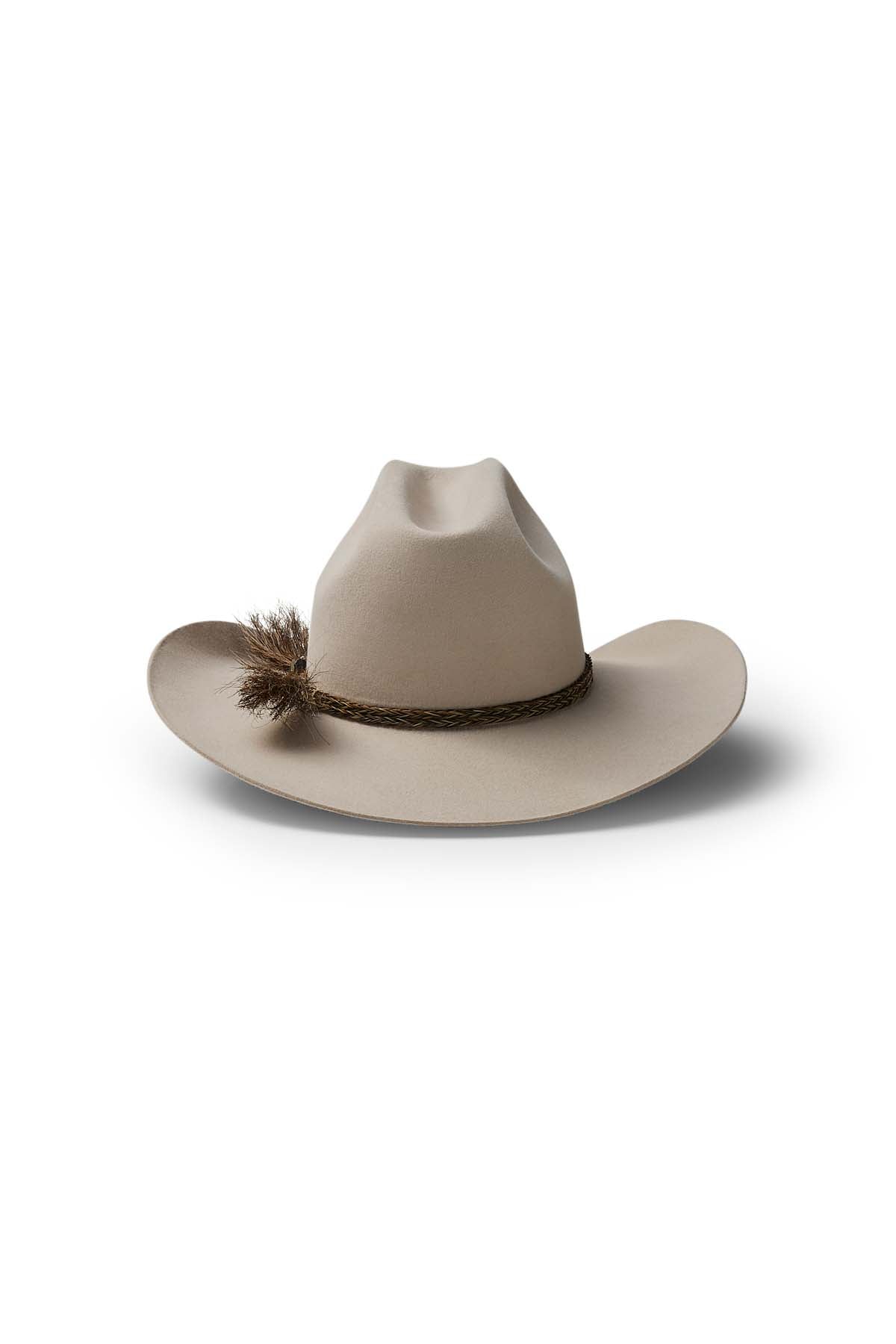 The Akubra Rough Rider is a beige, wide-brimmed cowboy hat featuring a braided band and brown feather tuft, displayed on a white background with a subtle shadow—an iconic, durable choice for adventure.