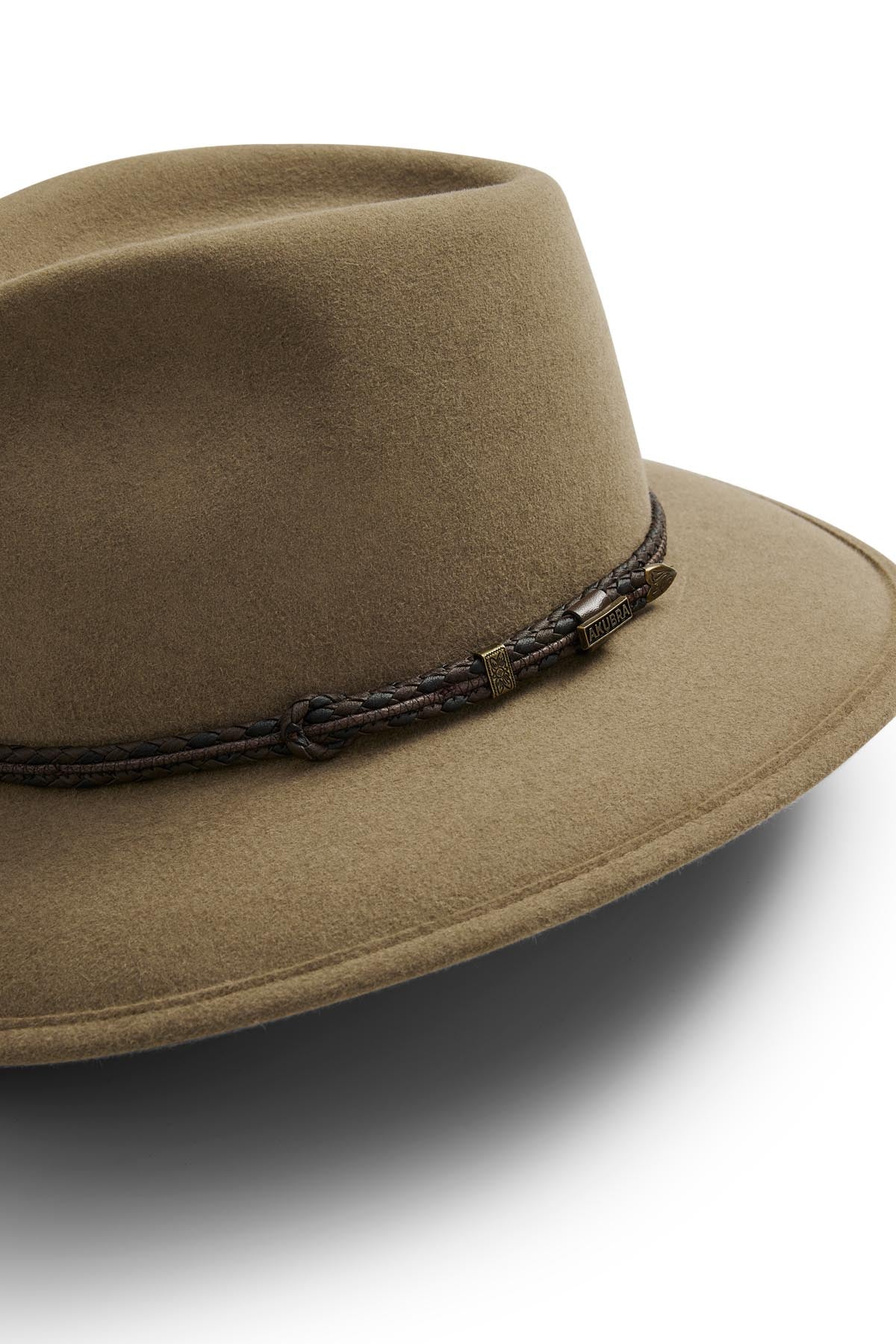 The Akubra Traveller is a brown hat with a wide, practical design, featuring a dark braided leather band and small metallic accent on the crown. Made from pliable felt, it's shown against a white background.