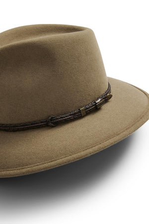 The Akubra Traveller is a brown hat with a wide, practical design, featuring a dark braided leather band and small metallic accent on the crown. Made from pliable felt, it's shown against a white background.