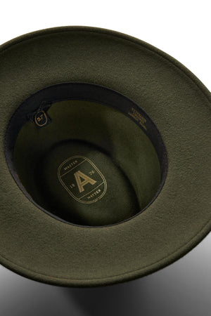 A close-up of the olive green Akubra Traveller hat's interior reveals its felt structure, black inner band, size label "57," and a gold logo with the letter "A," "MASTER," and "1876" on the lining.