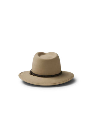 The Akubra Traveller is a tan felt hat with a wide brim, slightly dented crown, and dark braided band, showcasing its timeless design against a white background.