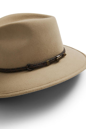 The Akubra Traveller is a tan hat with a timeless wide-brimmed felt design, accented by a dark braided leather band and small metallic details.