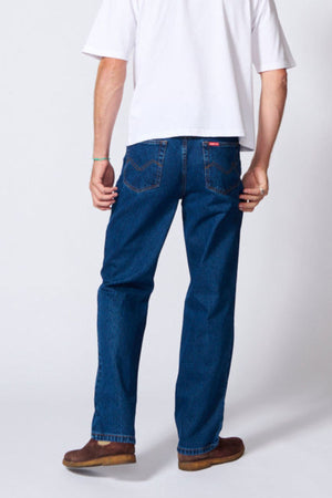 A person stands facing away, wearing a white T-shirt, brown shoes, and AMCO Rigid Regular Fit Jeans made from 100% cotton denim, with their right hand at their side and left hand relaxed.