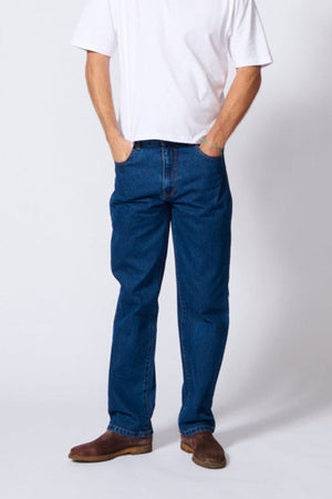 A person wearing a plain white t-shirt, AMCO Rigid Regular Fit Jean made from 100% cotton denim, and brown shoes stands with hands in their pockets against a plain light background. Their face is not visible.