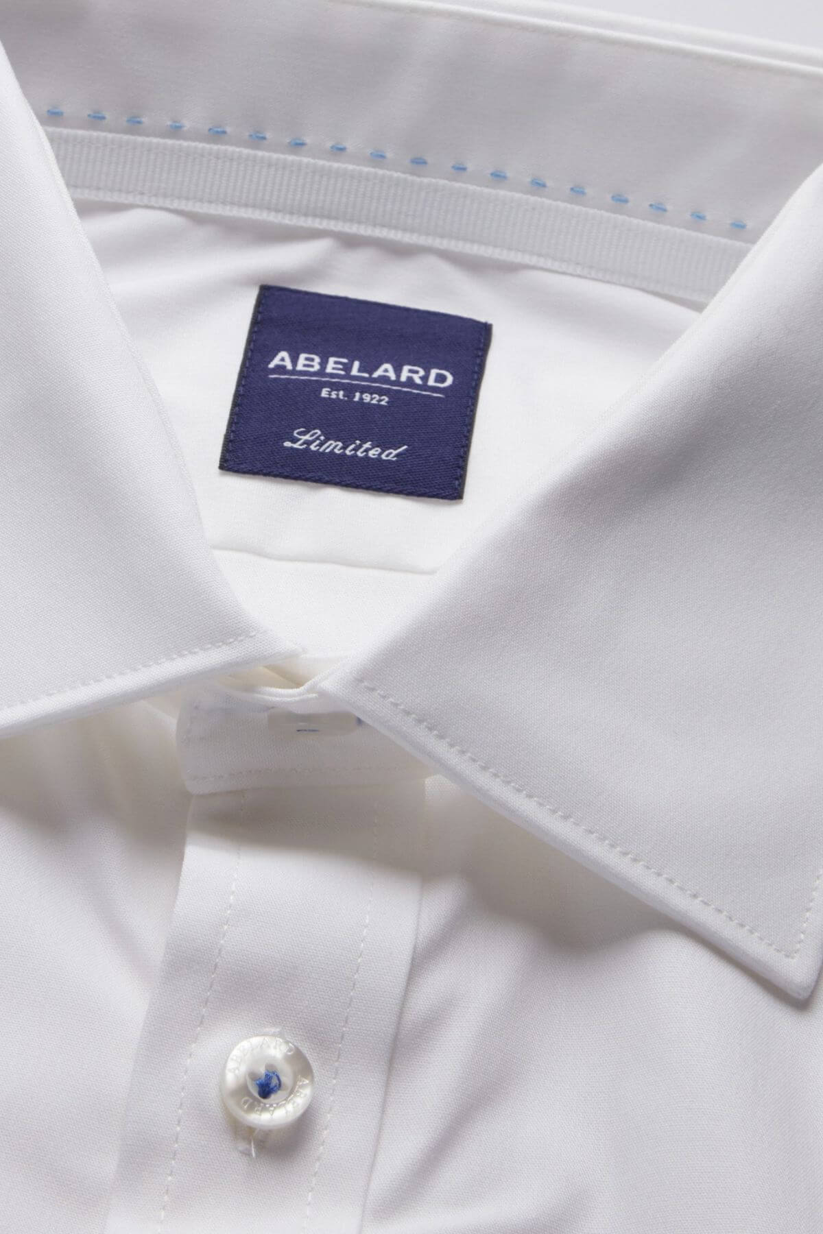 Close-up of a neatly folded white dress shirt with a label on the inside collar that reads "ABELARD Est. 1932 Limited." This Abelard 4 Way Stretch Poplin Slim Fit shirt is wrinkle-resistant and features a stiff collar, buttoned cuffs, and smooth, well-pressed fabric. Its Slim Fit design ensures you look sharp for any occasion.