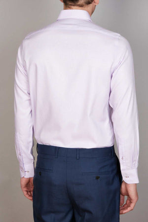 A person wearing an Abelard Non Iron Cotton Twill Slim Fit Shirt in light pink and navy blue dress pants is seen from the back. The shirt features a cutaway collar, long sleeves with buttoned cuffs, while the pants have buttoned back pockets. The individual is standing against a plain, light-colored background.