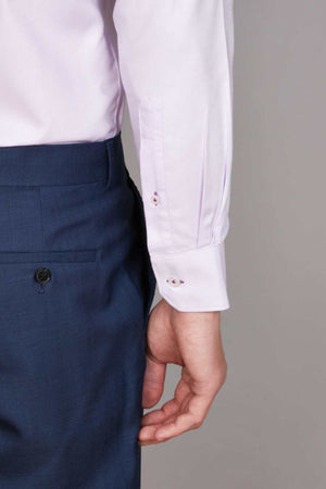 A person wearing an Abelard Non Iron Cotton Twill Slim Fit Shirt in light pink with a cutaway collar and dark blue dress pants is shown from the side, focusing on the midsection and arm. The hand is relaxed by their side, displaying double-buttoned cuffs on the shirt.