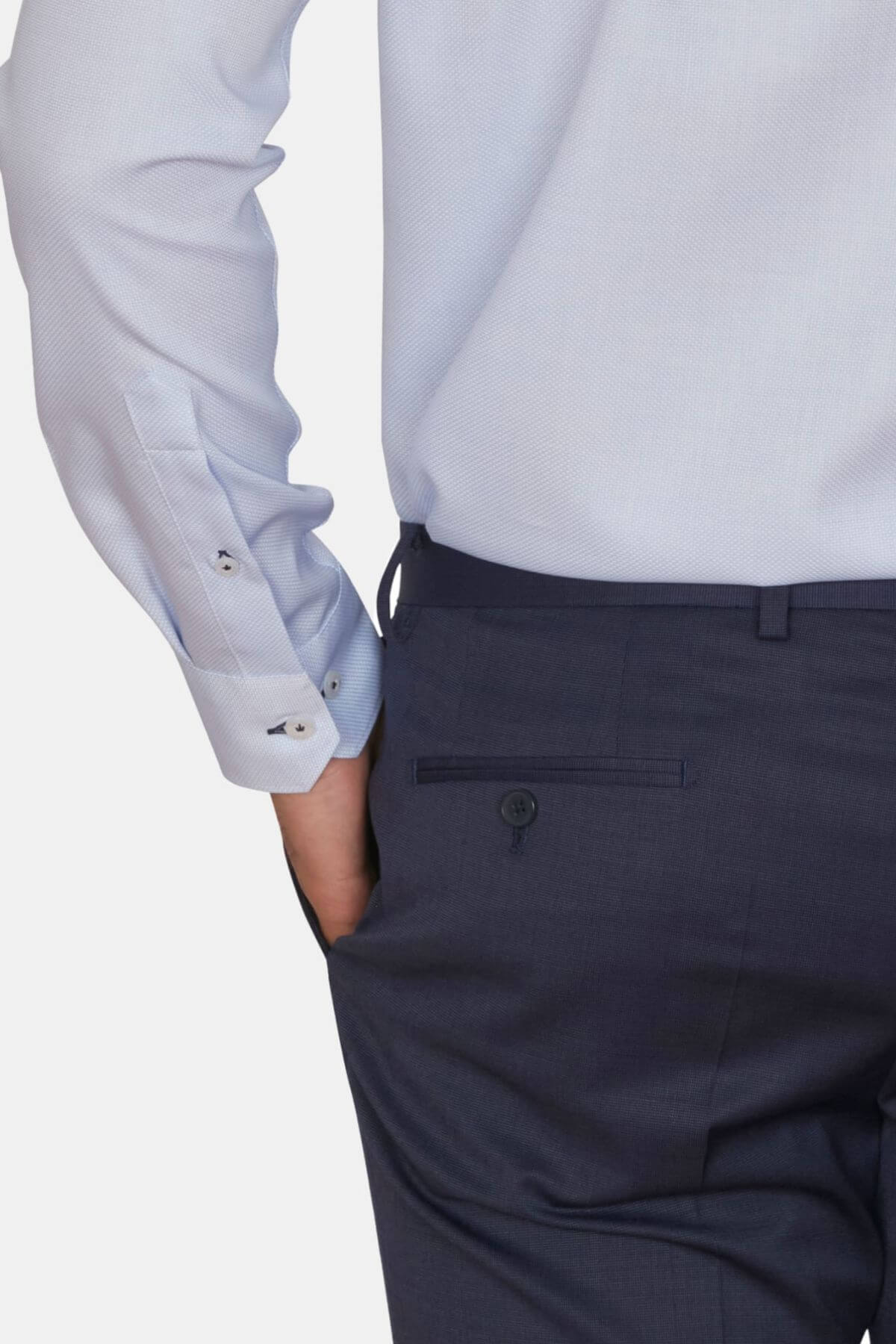 A person in a light blue Abelard Waffle Dobby Slim Fit Shirt with buttoned cuffs and dark trousers with a rear pocket has their hand in the pocket. The shot focuses on the back, highlighting the 100% cotton fabric's waffle dobby design and detailed craftsmanship.