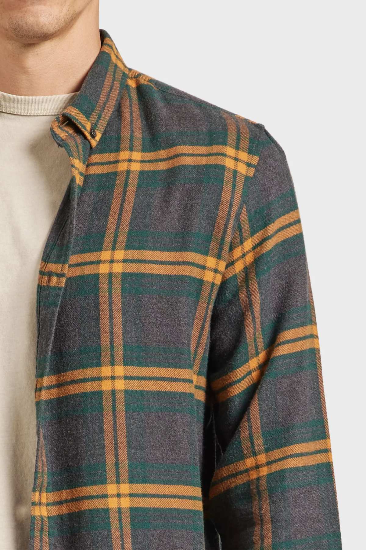 Someone is wearing an Academy Brand Denver Shirt in gray, green, and orange plaid over a beige t-shirt. The partially buttoned cotton shirt highlights a casual style against a plain light gray background.