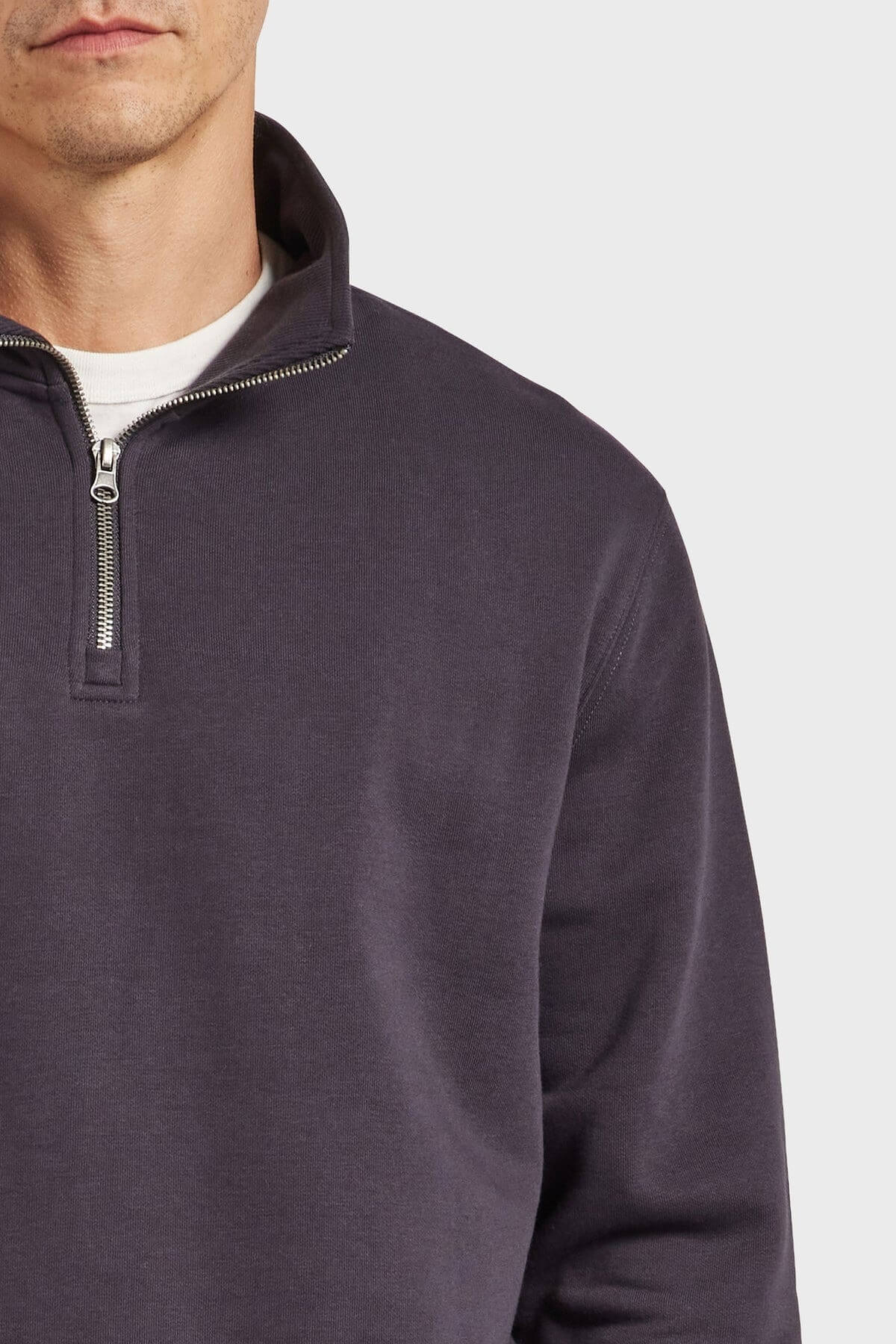 A man models the Academy Brand 1/2 Zip Sweat in dark gray over a white shirt, shown chest up against a plain light background, with only the lower half of his face visible.