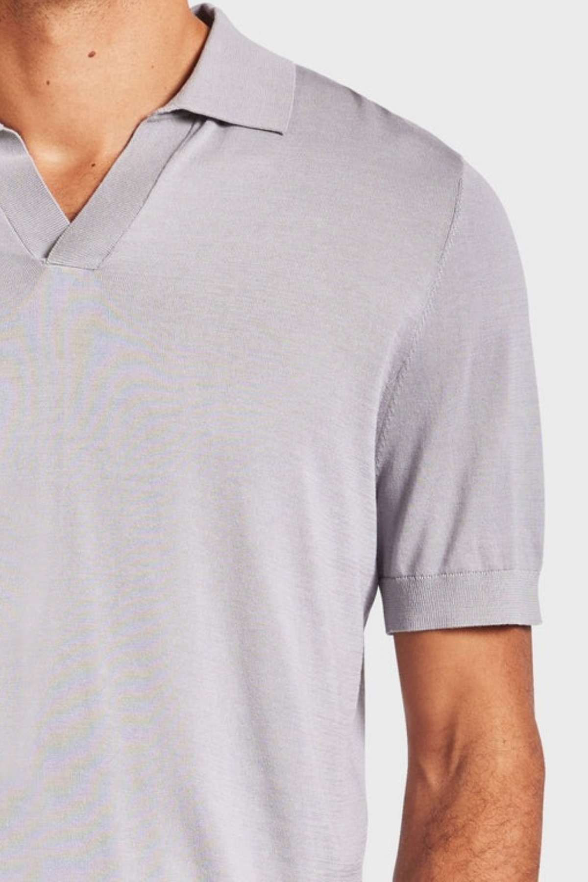 A person wearing a light grey, short-sleeved Academy Brand Irvine Knit Polo with a V-neck collar stands against a plain white background, visible only from the chest up.