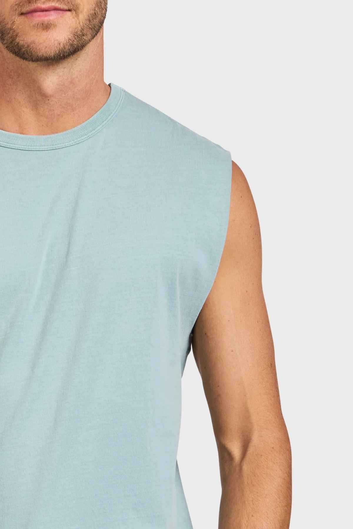 A person wearing a light blue Academy Brand Jimmy Muscle Tee is partially visible, showing their chest and left shoulder against a plain white background.