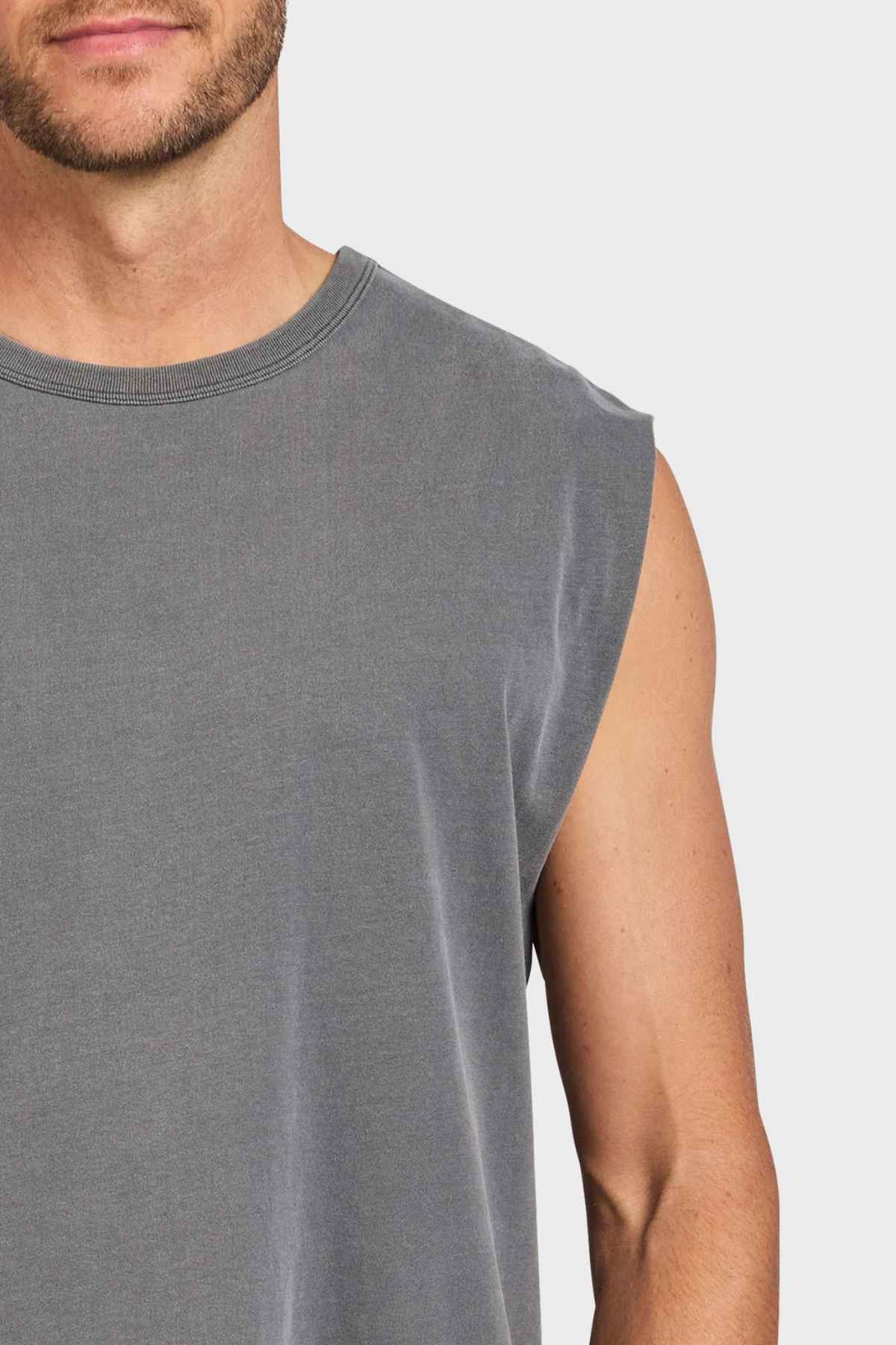 The image displays an individual from the shoulders down wearing the Academy Brand Jimmy Muscle Tee. This sleeveless gray tee, made entirely of cotton, showcases a round neckline set against a simple white backdrop.