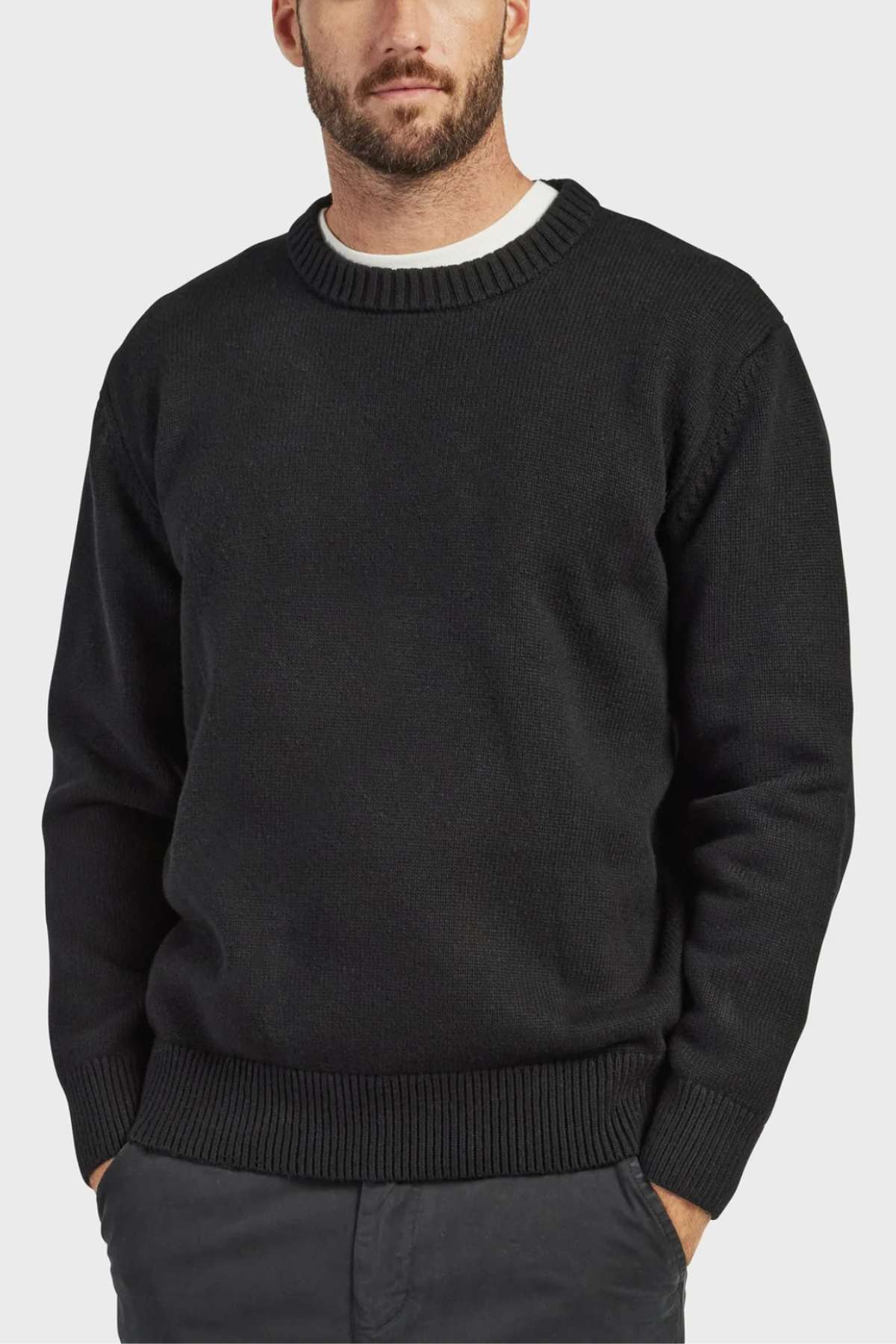 A bearded man dons a high-quality, black ribbed crew-neck sweater from the Academy Brand Malibu Crew Collection, paired with light gray pants. He stands against a plain white background, showcasing his cozy, stylish look.